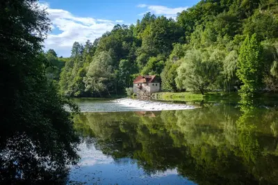 a house sitting on the shore of a river at Apartments Natura in Adlešiči