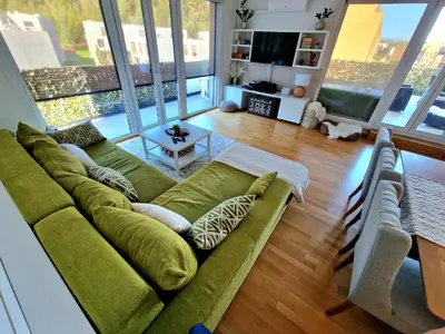 a living room with a green couch and large windows at Waldorf Apartment in Ljubljana