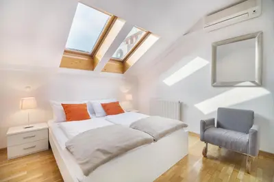 a white bedroom with a bed and a chair at City Central Ljubljana in Ljubljana