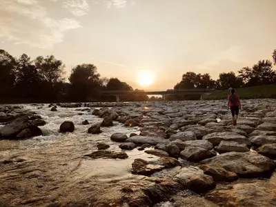 a man walking across a rocky river at sunset at Green Street Hideaway in Šempeter v Savinjski Dolini