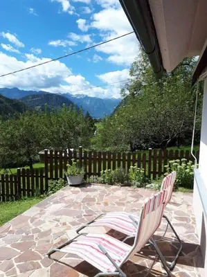 two chairs on a patio with a fence and mountains at Cottage Stela, family moutain hideout in Bohinj