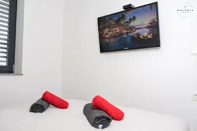 two red pillows on a bed with a tv on the wall at Meloria Apartments in Veržej