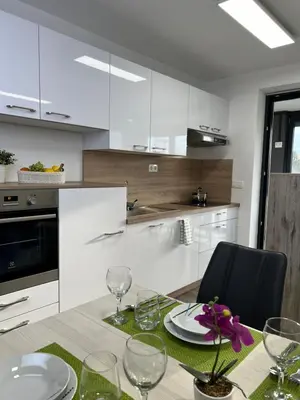 a kitchen with white cabinets and a dining table with glasses at Meloria Apartments in Veržej