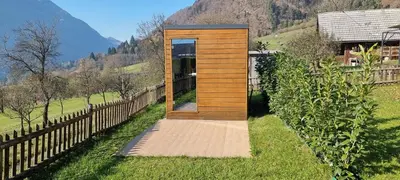 a wooden tiny house in a field with a fence at Via Alpina Apartments with sauna in Mojstrana