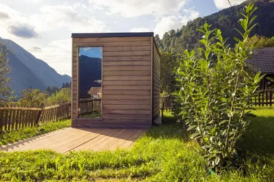 a small wooden cabin with a wooden deck at Via Alpina Apartments with sauna in Mojstrana