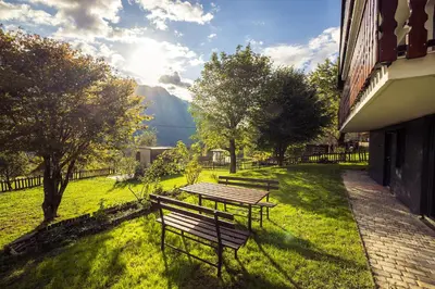 a picnic table and benches in a field with a mountain at Via Alpina Apartments with sauna in Mojstrana