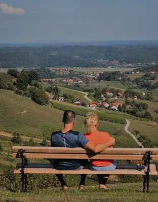 a man and woman sitting on a bench overlooking a valley at HERBALIJA Apartment Herbalija - sorrounded by Nature in Podčetrtek