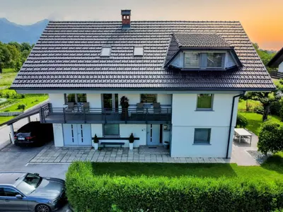 a white house with a roof with a car parked in front at Apartma Bled in Bled