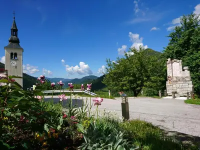 a church with a clock tower and a street with flowers at Kmetija Na Čendavš in Cerkno