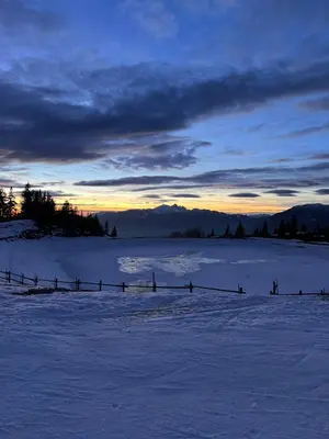 a fence in a snow covered field with a sunset at Alpine Escape Golte Apartment in Mozirje