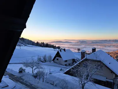 a house covered in snow with the sunset in the background at Apartma Maya in Cerklje na Gorenjskem