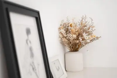 a white vase with flowers in it next to a picture at A modern flat in Kranjska Gora