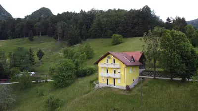 a yellow house on top of a green hill at Apartma pri Milki in Cerkno