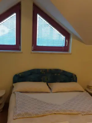 a bed in a bedroom with two windows at Hostel - Rooms Kaj & Kaja in Slivnica pri Mariboru