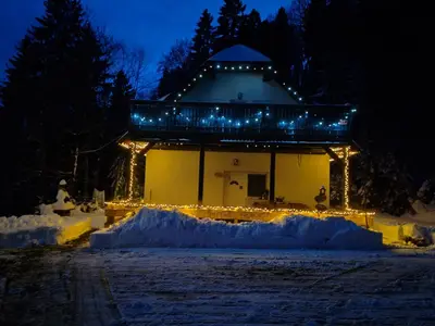 a building with lights in the snow at night at apartma Pohorc - Praprot in Pohorje