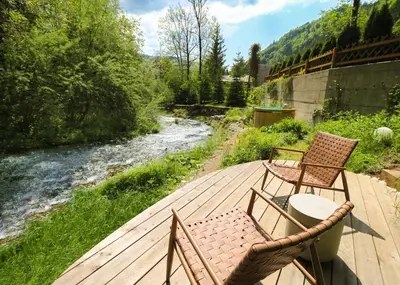 two chairs and a table on a deck next to a river at Designer Riverfront Cottage in Podljubelj