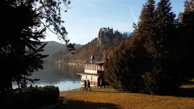 a building on the shore of a lake with a castle at Apartment Alpine Lake in Bled