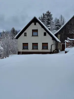 a house covered in snow in front of a barn at Apartma Hiška Vrh in Stari Trg pri Ložu