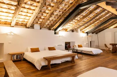 two beds in a large room with wooden ceilings at Vila Kobdilj 1835 Historic Homestead with Shared Courtyard in Štanjel