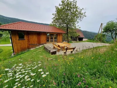 a wooden cabin with a bench in a field of flowers at Studio Apartma2 pri Adamu in Mislinja