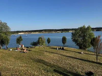 a group of people sitting on the grass near a lake at Apartma Rače in Rače