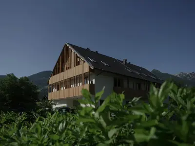 a building in a field with mountains in the background at Bohinj River House Spa&Sport in Bohinj