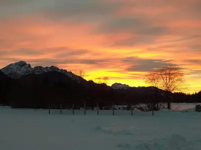 a sunset over a snowy field with a mountain at Apartma Confine in Rateče