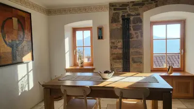 a dining room with a wooden table and two windows at Hiša Manira in Ajdovščina