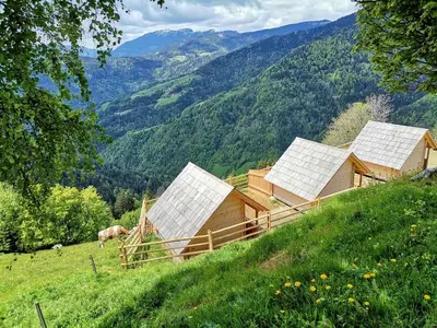 a group of barns on a hill with mountains at Scenic Glamping Huts with Mountain Views near Ljubno ob Savinji, Slovenia in Mozirska Koča