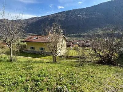 a house in a field with mountains in the background at Hisa Betin 4 bedroom Holiday Home in Soca Valley in Tolmin