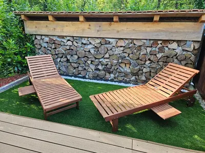 two wooden chairs and a bench next to a stone wall at Koča ob ribniku in Ponikva