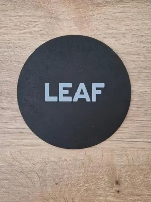 a black circle with the wordleaf on a wooden table at Linden Retreat Apartments with Sauna in Spodnje Mestinje