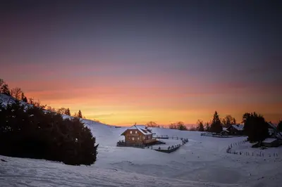 a cabin in the snow with a sunset in the background at Apartments Krvavec in Cerklje na Gorenjskem