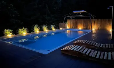 a swimming pool at night with two chairs and an umbrella at Vila Tin & Koča Tin in Prestranek