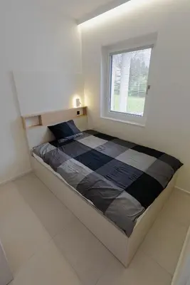a bed in a white room with a window at ALPEART GOZD MARTULJEK HOLIDAY unit in Kranjska Gora