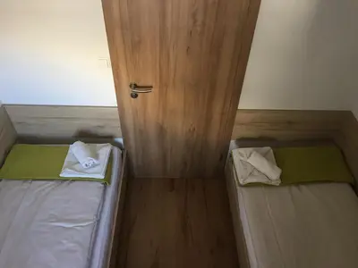 two beds in a small room with a door at Apartmaji in sobe Tina in Kranjska Gora