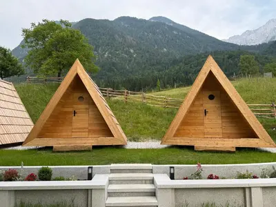 a group of three triangular dwellings with mountains in the background at Glamping Kamp Triglav in Soča