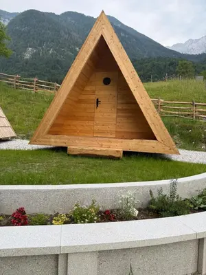 a triangular dog house in a field with mountains in the background at Glamping Kamp Triglav in Soča