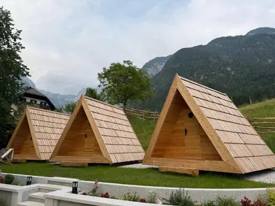 a group of three wooden structures with mountains in the background at Glamping Kamp Triglav in Soča