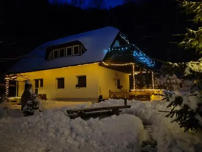 a house covered in snow at night with lights at apartma Pohorc - Kostanj in Pohorje