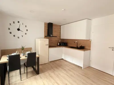 a kitchen with a table and a refrigerator and a clock at Apartments KrAnJ - City Studio Katka in Kranj