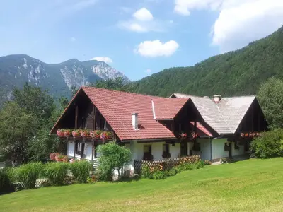a house with a red roof with mountains in the background at Turistična Kmetija Zgornji Zavratnik in Luče