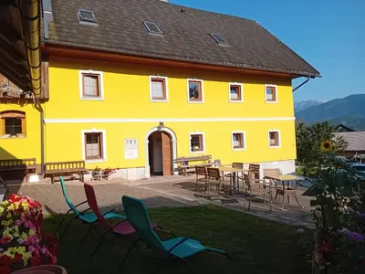 a yellow building with chairs and tables in the yard at Tubej apartments in Bohinj