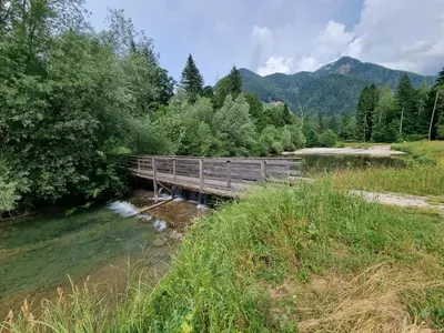 a wooden bridge over a river with mountains in the background at Luna's House in Zgornje Jezersko