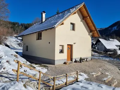 a white house with a wooden door in the snow at Luna's Mountain House - Jezersko in Zgornje Jezersko