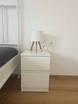 a white nightstand with a lamp on it next to a bed at Apartma DUDI