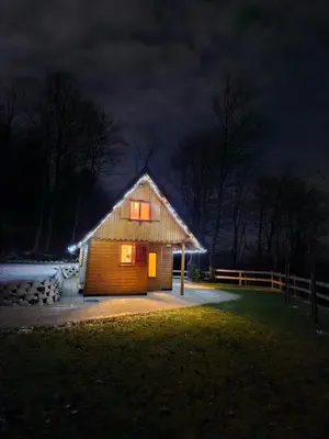 a small wooden cabin at night with lights on at Hiška pod krošnjami