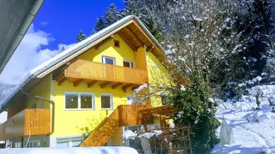 a yellow house with a balcony in the snow at Apartment Murka in Begunje na Gorenjskem