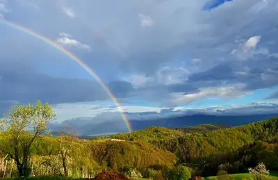 a rainbow in the sky over a valley with trees at Vineyard cottage Pri mali luži in Trebelno