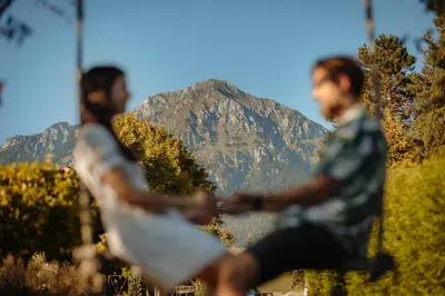 two men sitting on a bench with a mountain in the background at Glamping Bizjak in Preddvor
